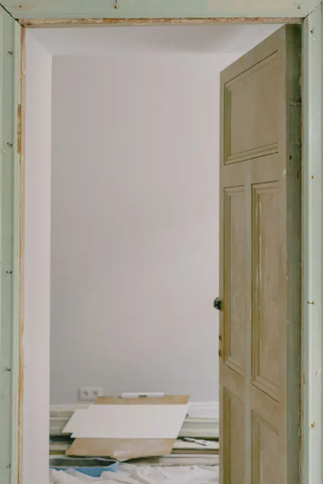 Porte ouverte sur une pièce en travaux, plaques et protections au sol